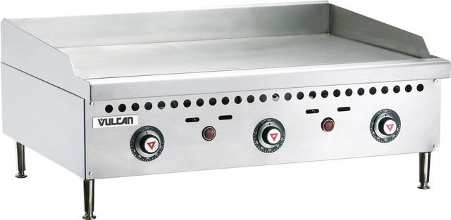 A 36 inch stainless steel countertop gas griddle with a polished steel griddle plate, three control knobs, indicator lights, and ventilation holes. The flat surface features raised back and side splash guards, four sturdy legs, and the Vulcan brand name.