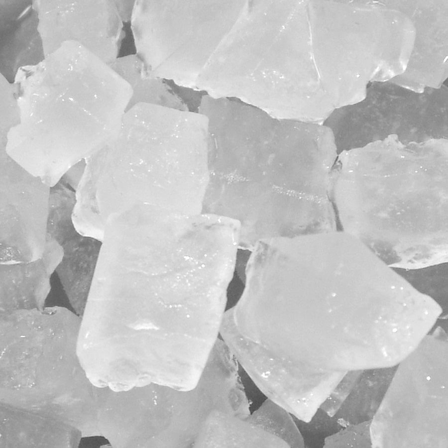 A close-up image of multiple translucent, roughly rectangular salt crystals. The jagged edges and stacked formations create a geometric surface, reminiscent of cubelet ice from an ice maker. The overall color is a frosty white with subtle shadows and highlights.