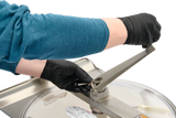 A person wearing black gloves and a teal long-sleeve shirt uses a metal tool to adjust a bolt on a Hobart Cutter Mixer with a stainless steel bowl and clear lid, focusing on the hand and hardware details. The background is plain and light.