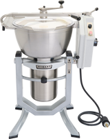 A large Hobart Cutter Mixer with a 45 qt capacity features a stainless steel bowl, transparent lid, button control panel, and black power cord coiled at the base, set on a sturdy four-legged metal stand.