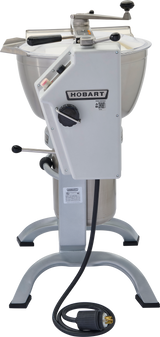 A commercial Hobart HCM450 Cutter Mixer features a large metal mixing bowl, control knobs, handle, and safety guards. It stands on a sturdy gray U-shaped metal base with a power cord and plug visible at the bottom.