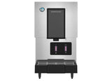 A stainless steel Hoshizaki ice maker Opti-Serve water dispenser features a black dispensing area, digital display, logo on the top left, and two buttons for ice and water above a drip tray. The machine stands on four short legs.