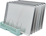 Five silver baking sheets are vertically organized in a Hobart rack with metal dividers. The light green rack base features an open lattice pattern, securely holding each sheet pan upright in a neat, evenly spaced manner against a white background.