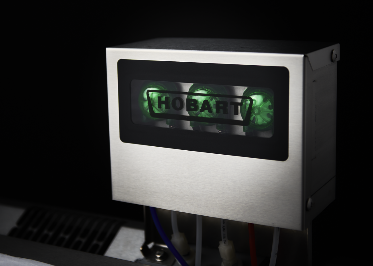 A metallic commercial dishwasher features a black-framed window displaying three green-lit dials and the word “HOBART.” Several colored wires are visible at the bottom, highlighting its chemical sanitizing functionality against a dark background.