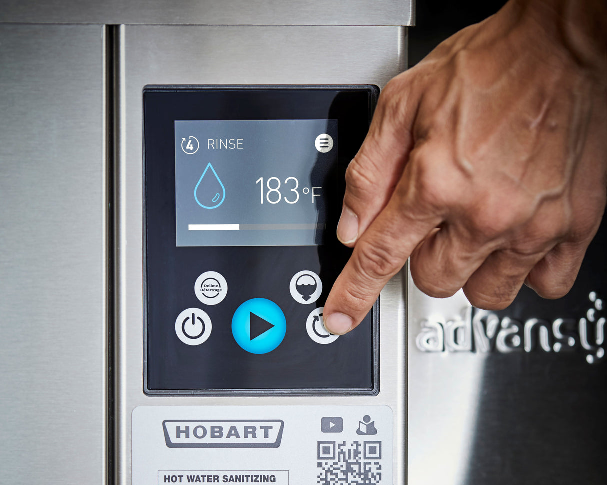 A close-up of a person’s hand pressing a circular button on a Hobart ventless dishwashing machine’s digital control panel, displaying a water drop icon, RINSE, and 183°F—showcasing high temp sanitizing and several touch buttons below.