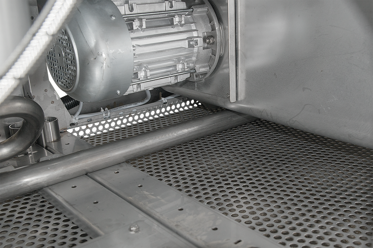 Close-up of an industrial metallic machine part featuring a cylindrical electric motor with ventilation holes, metal tubing, and a perforated floor grid—details common to a Hobart FT1000E flight type dish machine in a gray, utilitarian setting.