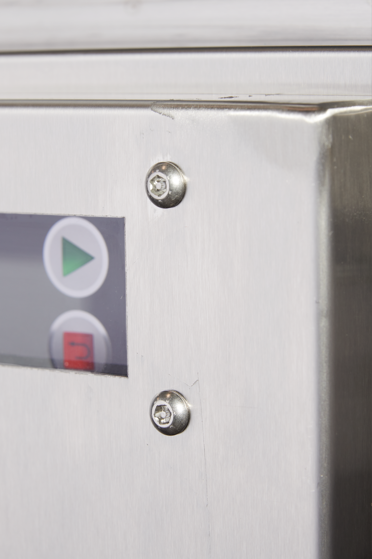 Close-up of a stainless steel control panel, likely from a ventless flight type dish machine. Two exposed screws and part of a display screen with play and stop buttons hint at advanced, low energy dish machine controls.