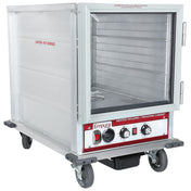 A stainless steel heated holding cabinet with 12 pan capacity sits on four wheels, its glass door open to reveal empty shelves. The front control panel features dials, switches, and indicator lights, with “Empura” branding visible.