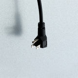 A black, three-prong electrical plug—perfect for a Reach-In Refrigerator—is shown against a light gray textured background. The plug is angled downward, with two flat prongs and one round grounding prong visible. The cord extends upward out of the frame.