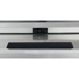 A rectangular black object sits centered on a stainless steel surface in front of a reflective glass panel. Behind the glass, a small dark rectangle with a round feature, possibly an Empura refrigeration sensor, is visible. The scene is minimal and industrial.