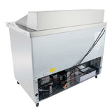 A commercial Empura refrigerated table is pictured from the back, showing exposed cooling components, wiring, a vented lower panel, and wheels. A black power cord hangs over the unit, with warning labels visible on the metal surface.