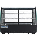 A front-facing, empty Empura countertop display case with three chrome wire shelves and a black base labeled “Empura.” Curved glass sides and a top LED light strip illuminate the interior. The background is plain white.