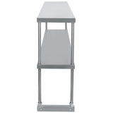 A stainless steel table viewed from the narrow end, featuring a smooth, reflective metallic finish, four cylindrical legs, and a lower shelf parallel to the tabletop—ideal for adding an optional table-mounted overshelf.