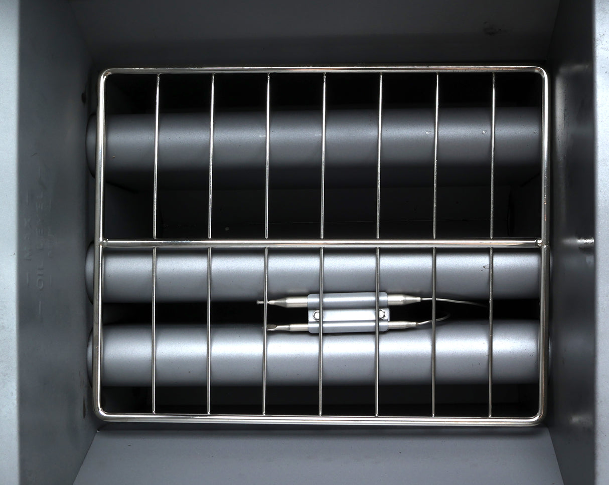 A close-up view of the inside of a commercial gas fryer, showing heating elements covered by horizontal metal rods and a removable wire rack at the front. The metallic gray surfaces and clean, industrial structure suggest durability and efficiency.