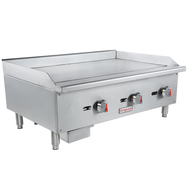 A stainless steel countertop griddle with three red and black control knobs, branded Empura. It has four sturdy legs, a flat cooking surface, raised side and back splashes, and a front-mounted grease tray beneath the controls.