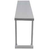 A long, rectangular stainless steel table viewed from the narrow end, featuring its smooth top surface and tubular metal legs with a horizontal support bar near the bottom. The industrial table could accommodate a convenient table-mounted overshelf for extra storage.