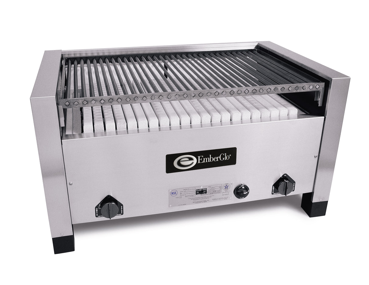 A commercial stainless steel charbroiler with parallel metal grates on top, a ceramic hearth of white briquettes beneath, and two black control knobs on each side. EmberGlo logo is displayed on the front center panel.