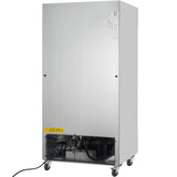 A large, upright commercial refrigerator with a plain silver front, ventilation and mechanical components visible at the bottom behind a black grille, four caster wheels for mobility, a yellow caution label on the lower left corner, and an electric cord extending out.