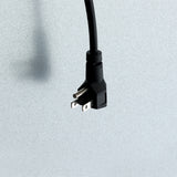 A black, three-pronged electrical plug hangs downward against a light gray, speckled background—reminiscent of those found on Empura Refrigeration units like a commercial freezer. The prongs face forward and the cord extends upward out of frame.
