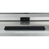 A rectangular black object sits centered on a stainless steel surface in front of a reflective glass panel. Behind the glass, a small dark rectangle with a round feature, possibly an Empura refrigeration sensor, is visible. The scene is minimal and industrial.