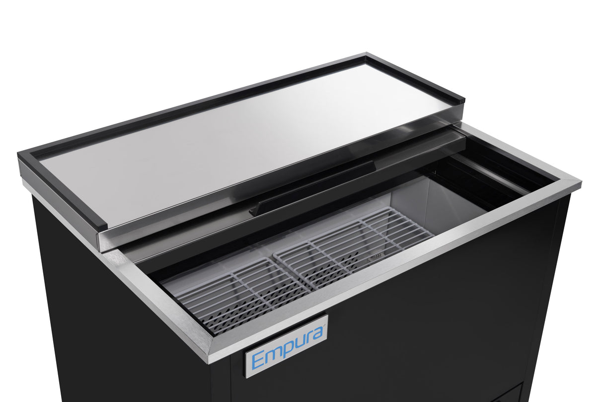 A commercial black chest freezer from Empura Refrigeration features a sliding stainless steel lid, partially open to reveal interior wire racks. The front showcases a blue and white Empura logo, highlighting quality Stainless Steel Refrigeration.