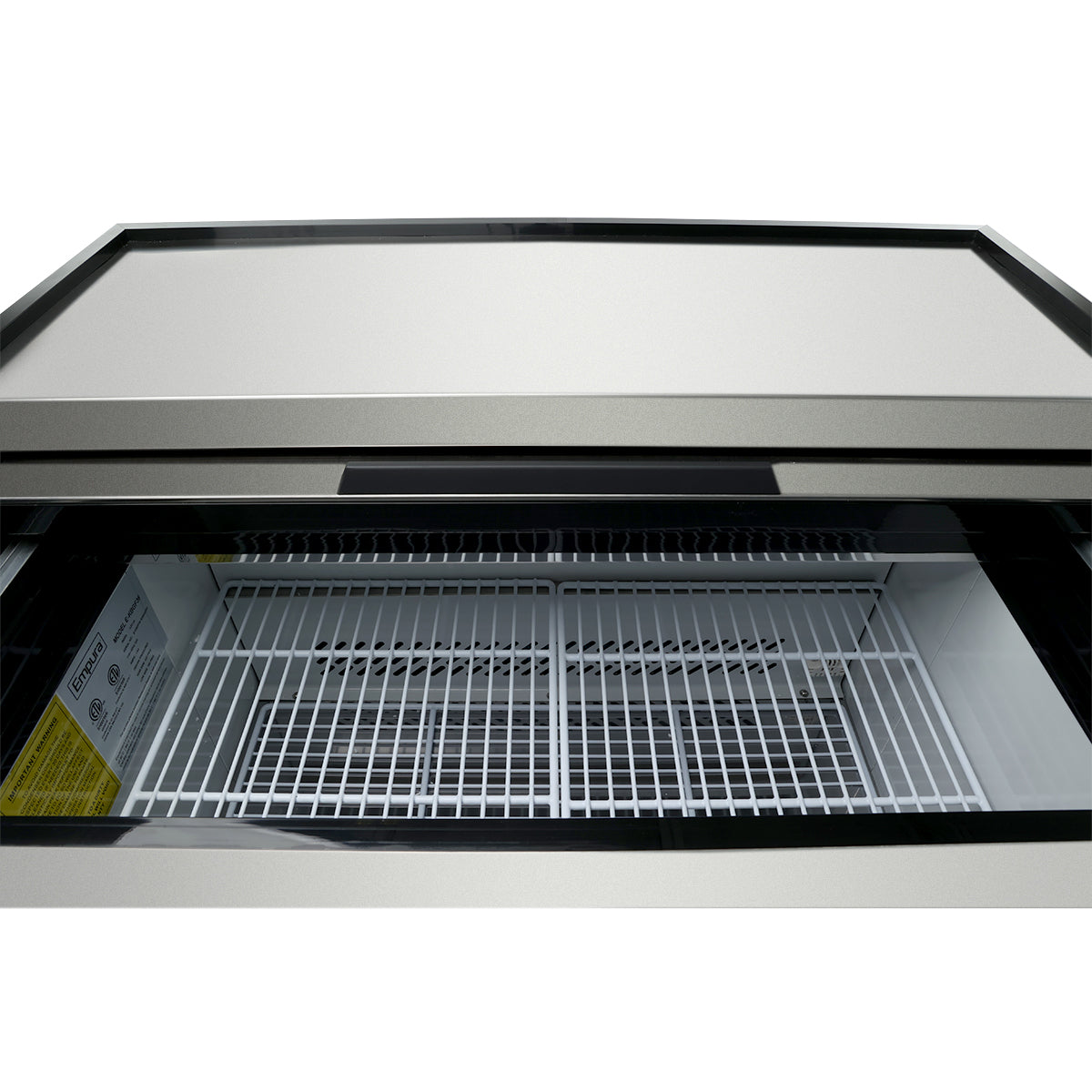 A close-up view of an empty commercial freezer with a glass top. The inside features white metal wire shelving, and there is a product information label along the interior wall. This glass door freezer is clean and well-lit.
