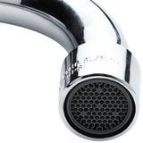 Close-up of a shiny, chrome wall mount faucet spout with a black aerator at the tip. The aerator has a honeycomb pattern, and some engraved text is partially visible on the metal near the end. The background is plain and uncluttered.