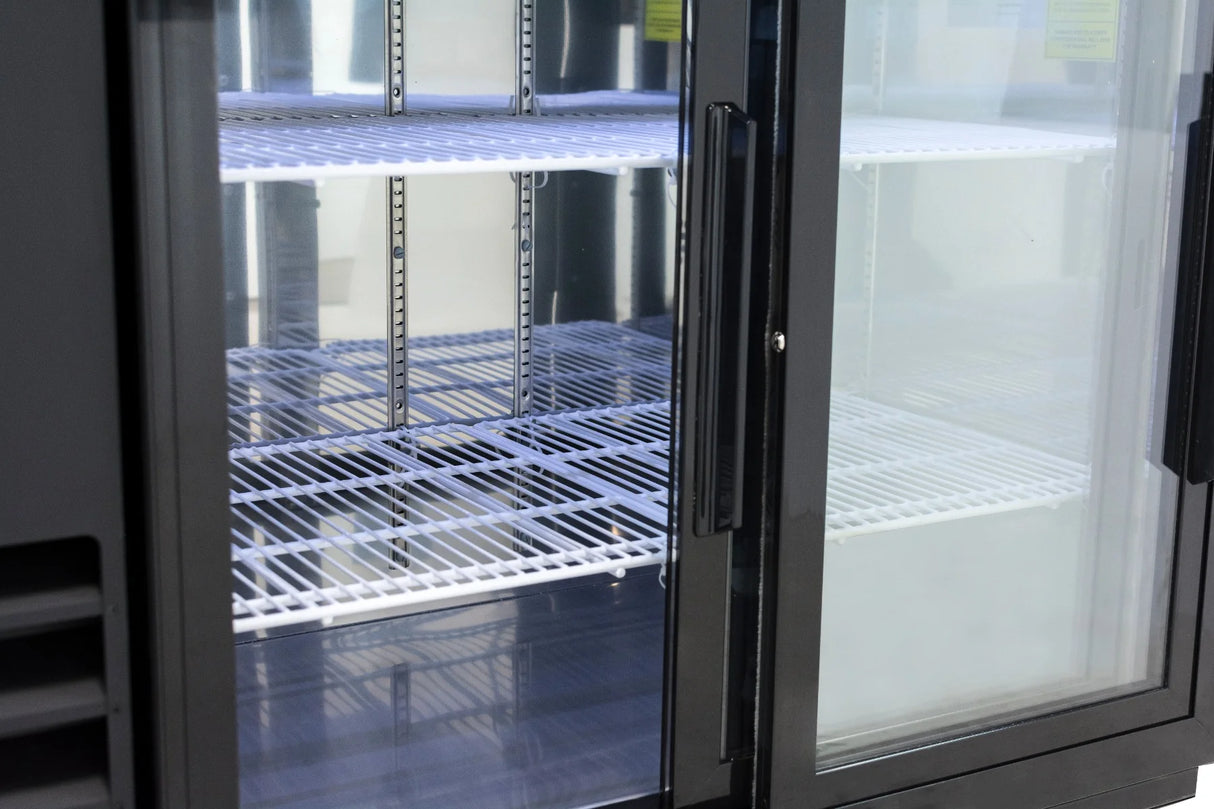 A commercial refrigerator with sliding glass doors stands open, revealing empty white wire shelves inside. The shelves are clean and evenly spaced, and the interior is brightly lit. No products or items are visible inside this commercial refrigeration unit.