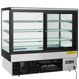 A commercial refrigerated display case with sliding doors, three glass shelves, and bright LED lighting. The lower section houses the cooling mechanism, visible through a vented panel with a yellow caution sticker and control panel on the front lower right corner.