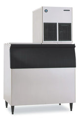 A Hoshizaki Ice Maker featuring a stainless steel body, large black front panel, and box-shaped top unit with two black ventilation grilles. This commercial flake-style machine stands on four short legs and sports a small logo in the upper left corner.