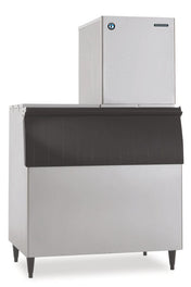 A commercial stainless steel Hoshizaki ice maker, featuring a boxy flake-style unit on top and a large storage bin below with a black, ridged front panel and four sturdy legs—perfectly designed for industrial or restaurant use.
