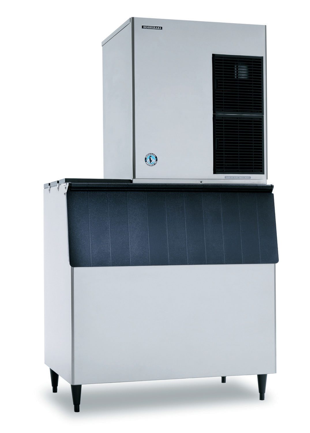 A large, commercial Hoshizaki ice maker with a rectangular silver body, black vent on the top right, and a black front bin lid. The unit stands on four black legs and has a blue circular logo on the front lower section.