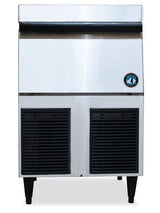 A Hoshizaki commercial ice maker with a stainless steel exterior, black vented panels at the bottom, four black legs, and a circular blue and white logo on the right side. The rectangular machine features a modern design and produces flake-style ice.