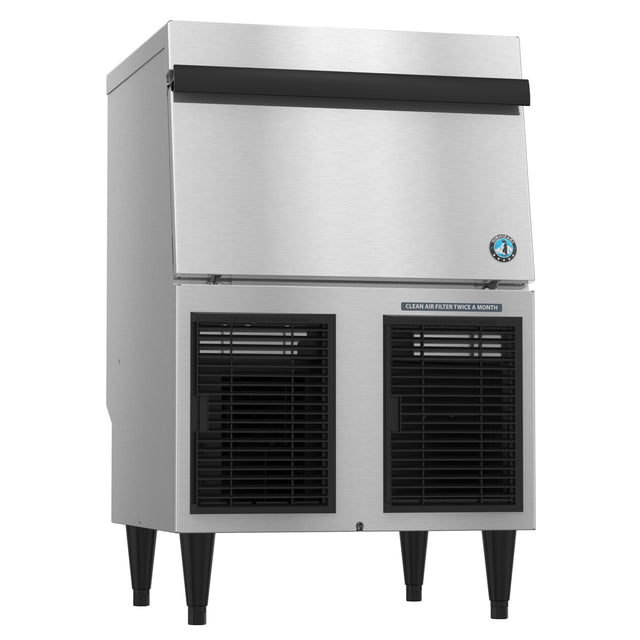 A commercial Hoshizaki stainless steel ice maker with a large front bin, black vented panels at the bottom, black top handle, and four black legs. A blue sticker and a label reading “CLEAN AIR FILTER TWICE A MONTH” are visible on the front.