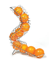 A modern, spiral-shaped Chrome Plated Fruit Basket by TableCraft is filled with bright oranges. The S-shaped holder balances on three legs against a plain white background, with the oranges neatly lined up inside the curved wire structure.
