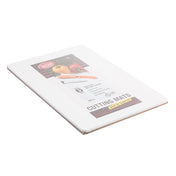 A white polyethylene cutting mat is shown still in its packaging. The label features images of a knife, tomato, and onion, and notes it is dishwasher safe. The rectangular mat measures 6 in x 9 in and lies flat on a white surface.