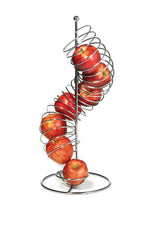 A modern chrome plated TableCraft fruit basket stands upright, holding several red apples stacked along its curved coil. One apple rests at the base, while others are distributed evenly throughout the spiral against a plain white background.