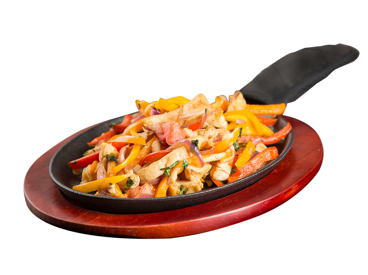 A sizzling Cast Iron Sizzle Platter filled with cooked chicken strips, colorful bell peppers, onions, and herbs sits on a wooden serving board. The handle is covered with a black protective sleeve, set against a white background.