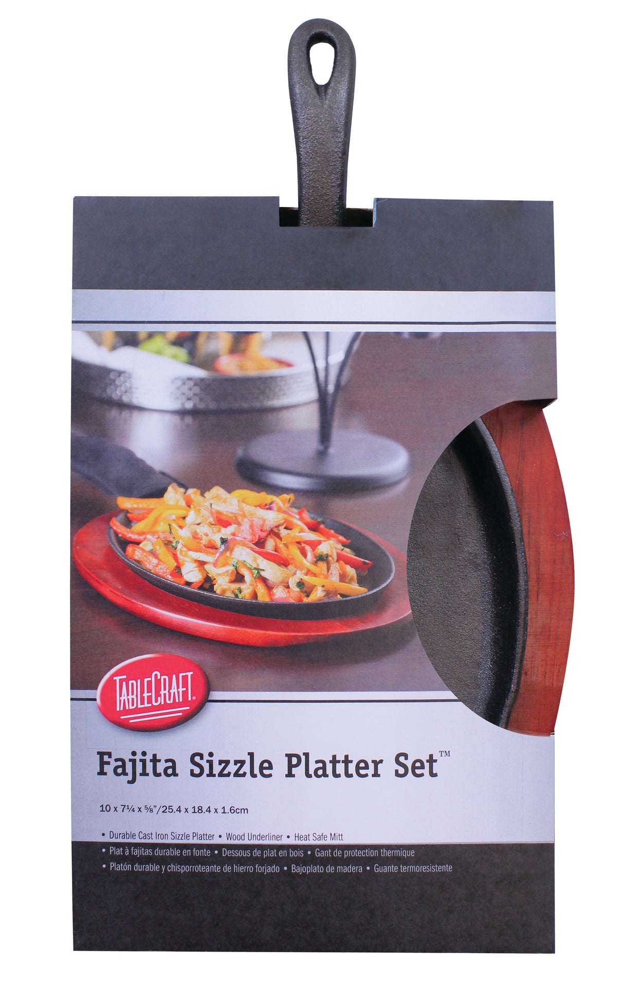 A TableCraft Products fajita sizzle platter set in packaging, showing a cast iron sizzle platter, wooden underliner, and handle mitt. The box features an image of fajitas on the platter and product details. The handle extends from the packaging top.