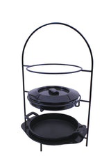 A black metal stand with two shelves holds a round lidded Dutch oven, perfect as a tortilla warmer, on the top shelf and a cast iron fajita platter on the bottom. The tall arched frame features a simple, minimalist design set against a white background.