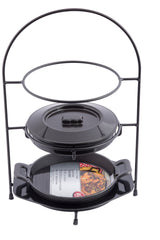 A black metal Fajita Tower Kit holds a round lidded cast iron Dutch oven above and a shallow cast iron fajita platter with handles below, displaying a paper insert with cooked food imagery. The background is white.