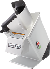 A commercial Hobart food processor with a stainless steel body, a large angled continuous feed chute, a black handle, a warning label, and two round buttons—one red and one green—on the side. The machine is standing on a flat, white surface.