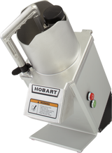 A metal Hobart Food Processor with a handle, chute for continuous feed, and safety lid. The front panel has the Hobart brand, a warning label with hazard symbol, and red stop and green start buttons. The machine is tilted slightly backward.