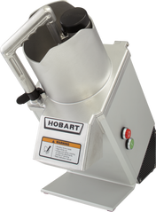 A metal Hobart Food Processor with a handle, chute for continuous feed, and safety lid. The front panel has the Hobart brand, a warning label with hazard symbol, and red stop and green start buttons. The machine is tilted slightly backward.