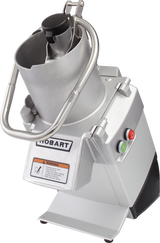 A commercial stainless steel food processor with a metallic finish, labeled “Hobart.” It features a cylindrical continuous feed chute with pusher, safety bar, red and green buttons, yellow warning label, and a sturdy base for heavy-duty kitchen use.