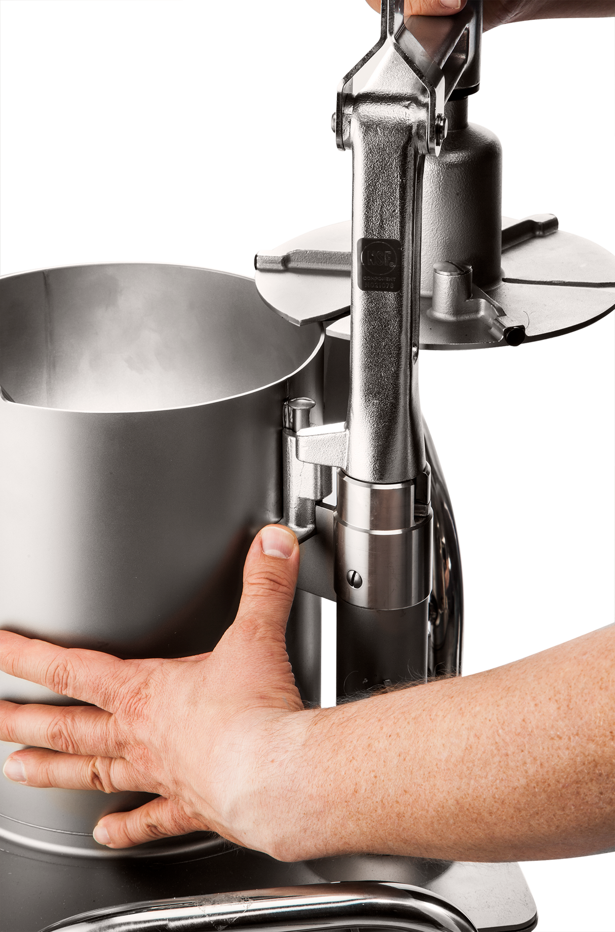 Close-up of two hands operating a high production food processor, with one hand steadying the cylindrical container while the other pulls down a lever attached to a disc, likely for slicing or pressing food inside.