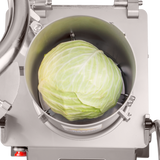 A whole green cabbage sits inside a Hobart FP400I Continuous-Feed Food Processor, viewed from above. The cabbage is centered in the clean, industrial chamber, surrounded by sharp blades ready for 132 lb/minute production.