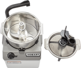 Top-down view of a silver Hobart Food Processor with its COOLCUTTER knives visible inside the 6 qt. bowl. The bowl is open, and the transparent plastic lid with black handles and feed tubes is placed to the right of the machine.