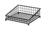 A black powder coated metal, square-shaped wire mesh tray with a grid pattern, raised edges, and four rounded feet. Part of the Grand Master Collection Basket by TableCraft Products, it’s designed for holding items like napkins or papers.