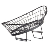 A modern black wire fruit basket shaped like a canoe or boat, featuring an open grid design and resting on two angled wire supports. This minimalist food pan basket allows air circulation around stored fruit.